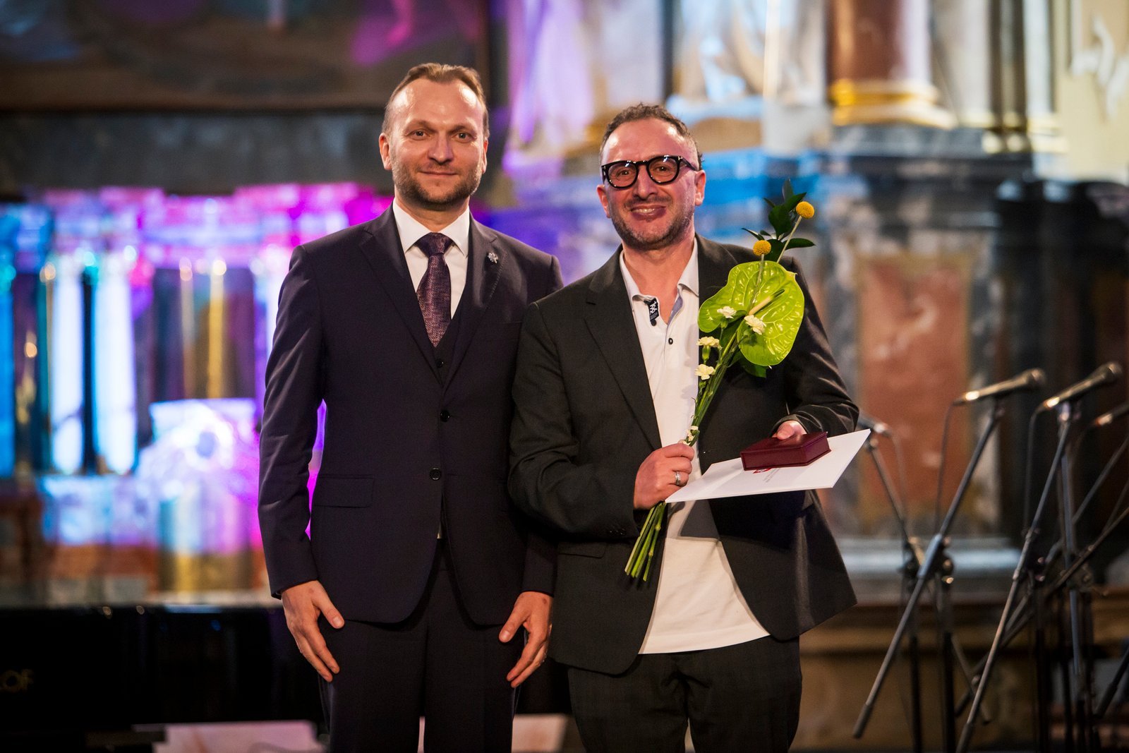 Ernest Alesin scenoje apdovanojimų renginyje su gėlėmis ir diplomu